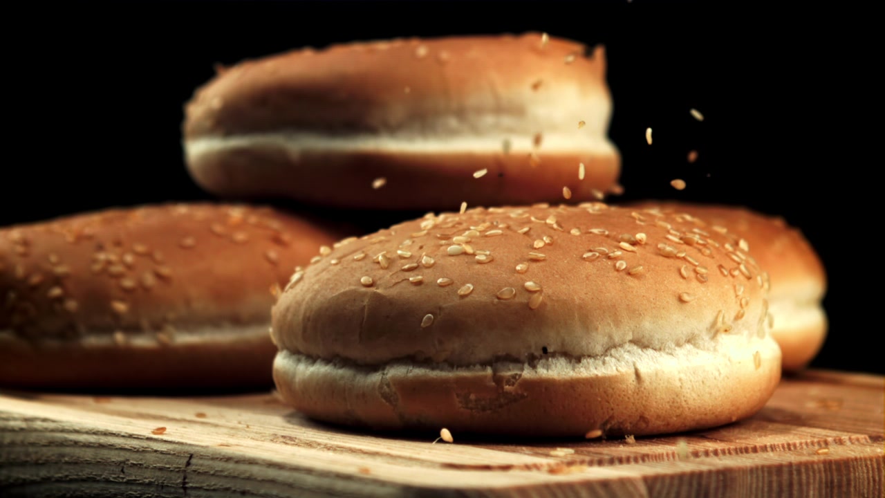 Sesame Seeds Falling onto Fresh Hamburger Buns in Slow Motion