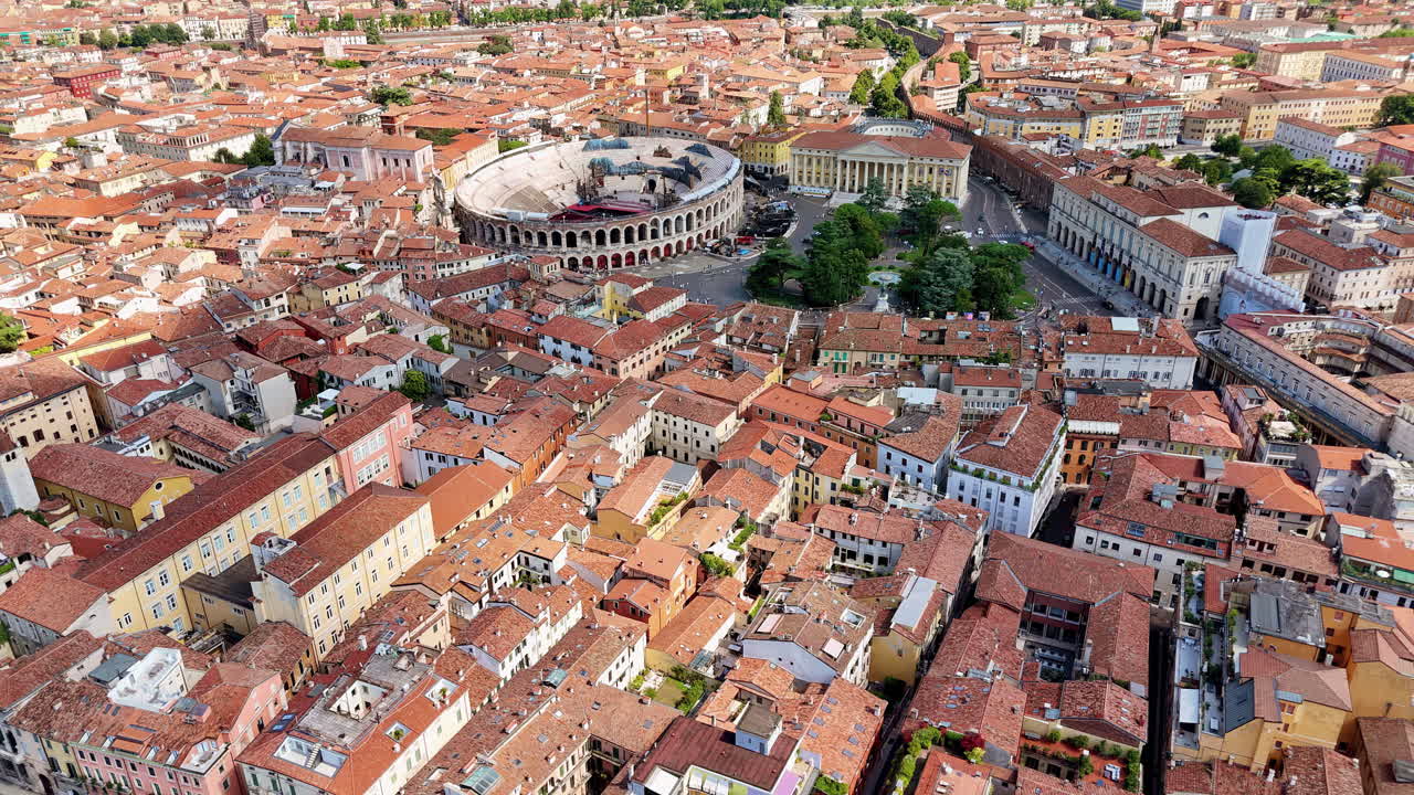 Vista aerea con drone del centro storico di Verona verso l'antico anfiteatro dell'Arena Romana, circondato da edifici colorati e strade cittadine.