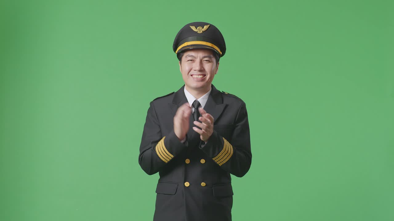 아시아인 조종사가 녹색 스크린 배경 스튜디오에 서서 미소 짓고 손을 치고 있습니다.