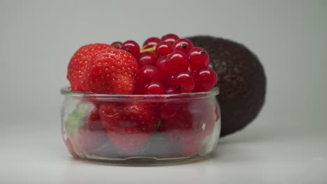 ripe avocado, strawberries and red currants in a clear glass bowl rotating- close up shot