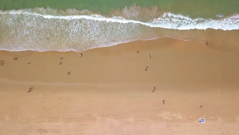 Turistas-Caminando-En-La-Orilla-Arenosa-De-La-Playa-Con-Olas-Oceánicas-Durante-El-Verano-En-Cabo-Trafalgar,-Cádiz,-España