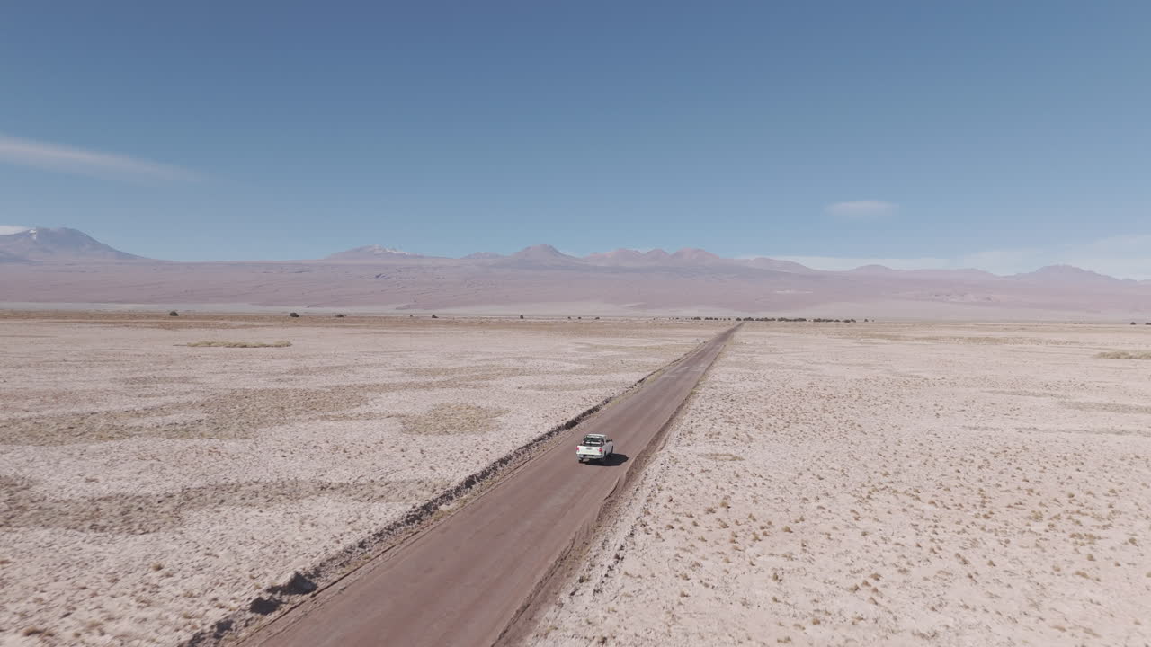 Drone shot flying over the dry sand desert mountains in San Pedro de Atacama Chile South America on a blue sky day with a white truck driving along near Mars Valley and Valley de la Luna LOG