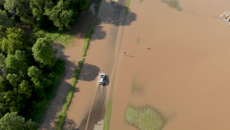 4k aerial following view of a car driving through flooding on a road outside of a town