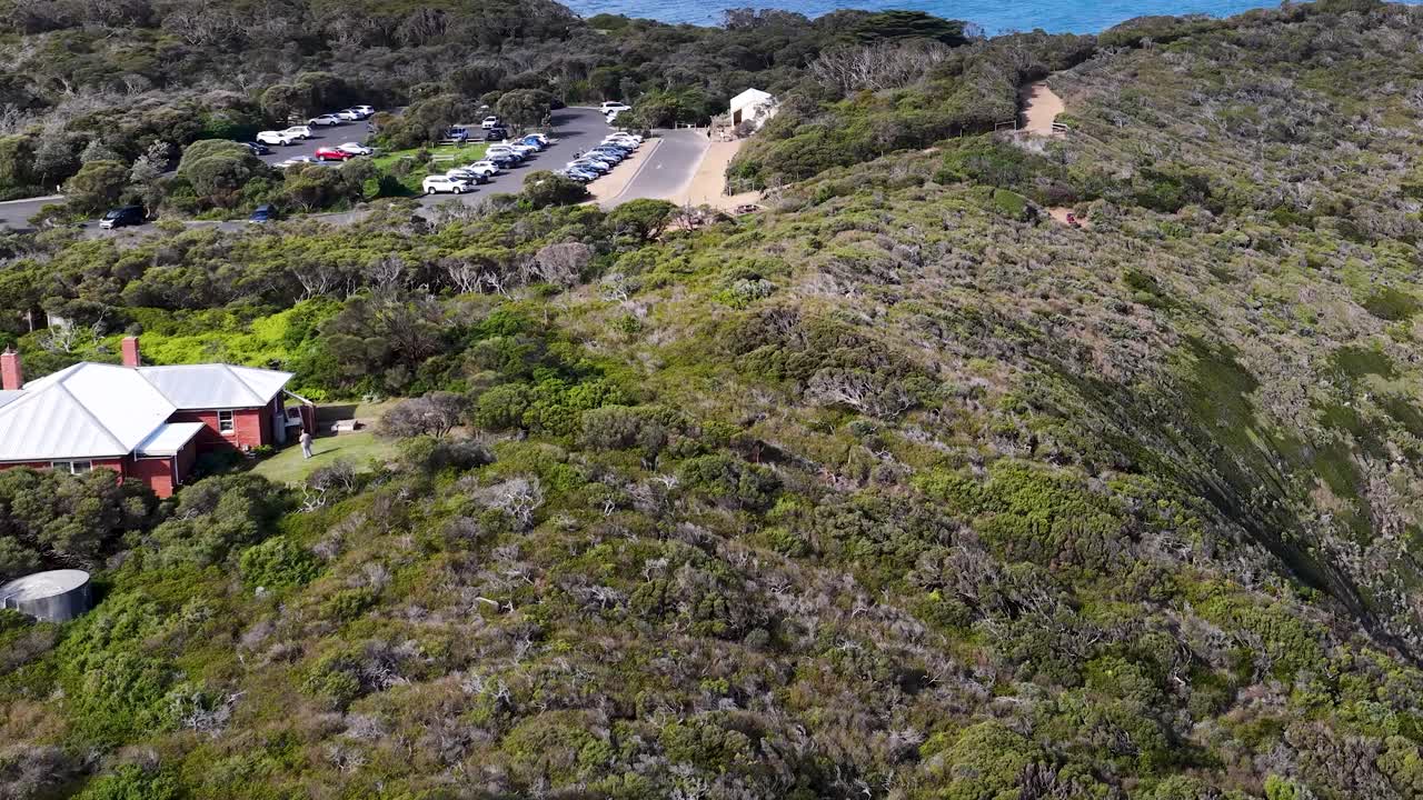 Drone glides past white lighthouse atop rugged cliffs, revealing lush greenery and coastal landscape