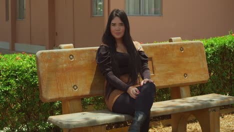 una joven hispana se sienta en un banco del parque, su cabello se balancea graciosamente en la suave brisa, mientras saborea la atmósfera tranquila a su alrededor