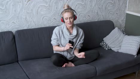 adorable middle aged blond woman sitting on sofa in her home and listen to the music