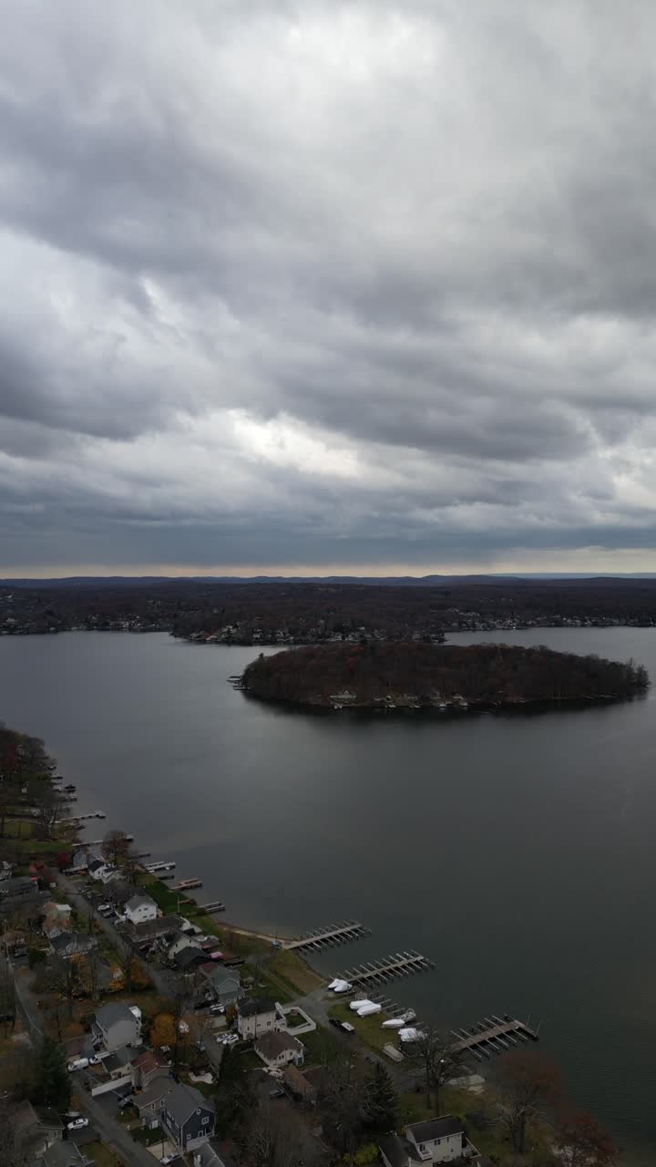 Low altitude drone flight over Larchmont’s lakeside showing a bay with houses, piers, and rich autumn foliage. Dramatic cloudy skies reflect on the water. Ideal for real estate or location B-roll