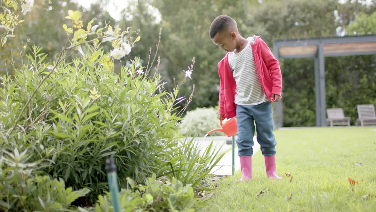 niño afroamericano regando plantas en el jardín en cámara lenta