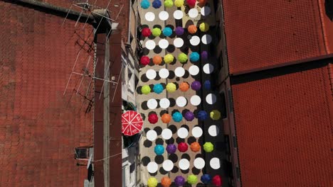 Aerial-View-Of-Colorful-Umbrellas-Along-Shopping-Urban-Street-On-A-Sunny-Day-In-Summer