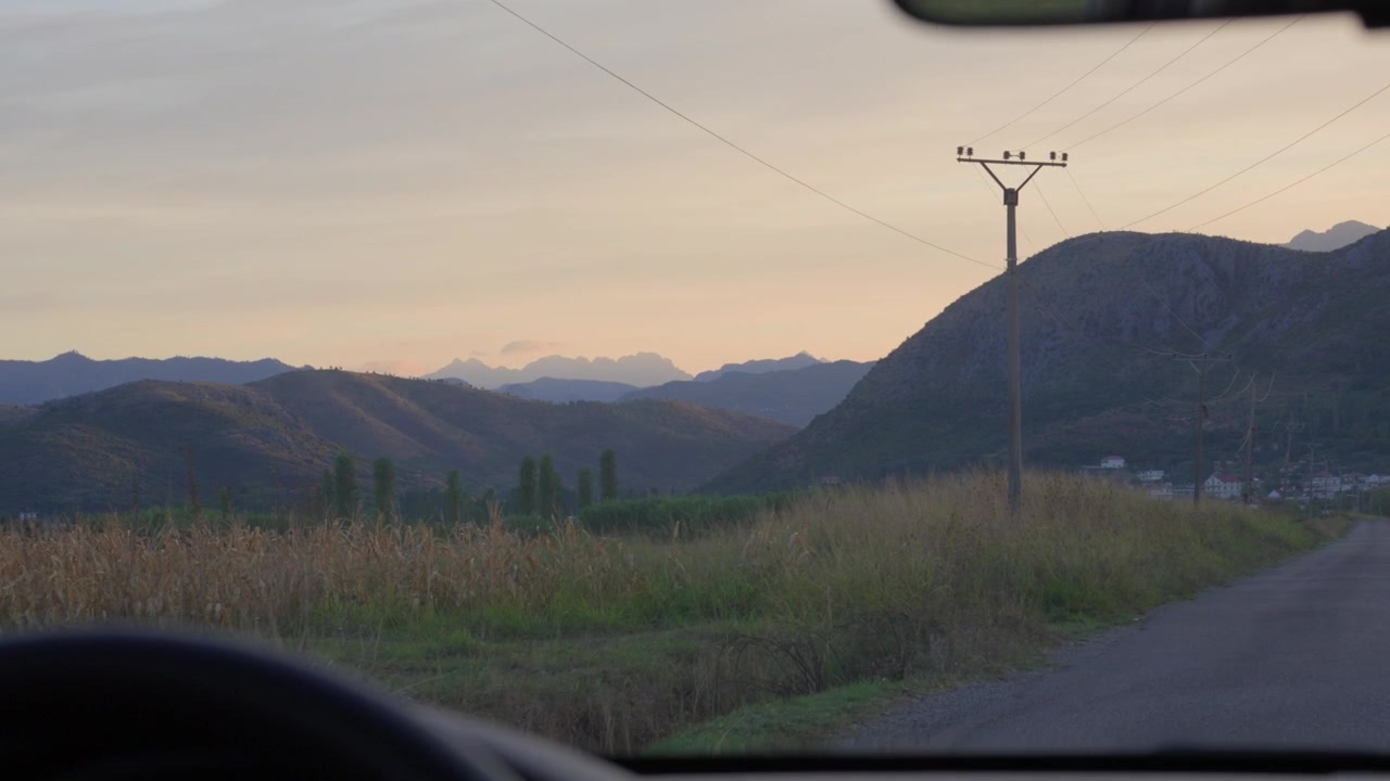 A peaceful drive through grassy fields and rolling hills at dusk, with soft fading light revealing the Drin river valley near Shkodër, Albania.