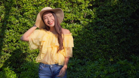 static shot of a beautiful asian lady wearing a summer hat, yellow top and jeans turning around while smiling at the camera