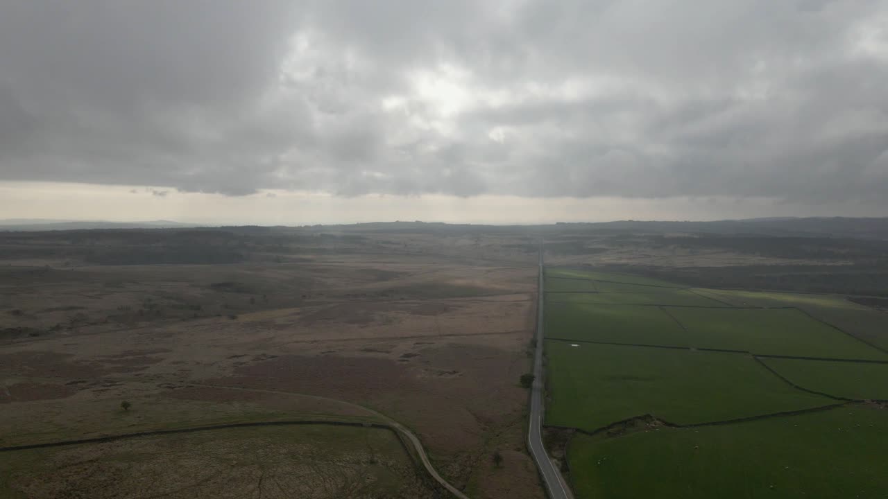 imágenes aéreas de drones que revelan un camino largo y recto a través de campos abiertos y páramos con un cielo nublado dramático