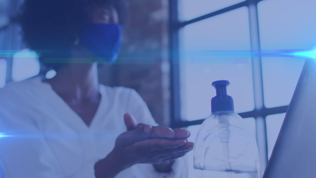 video compuesto de rastros de luz azul contra una mujer afroamericana que usa desinfectante para manos en una cafetería