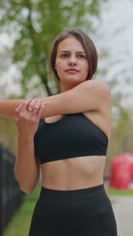 Athlete performing fitness exercises outdoors, stretching arms with blurred trees and iron fence in background, lively atmosphere, and playful game decoration in park