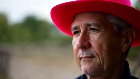 close-up portrait of a pensive senior man wearing a bright pink hat