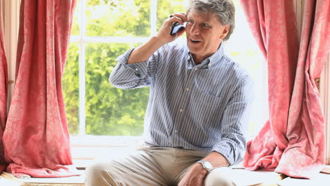 Mature-man-sitting-by-a-window-having-a-phone-call