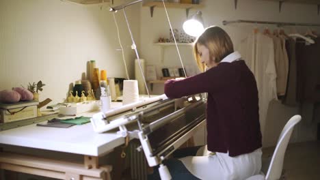 creative woman making knitted textile on loom machine in workshop