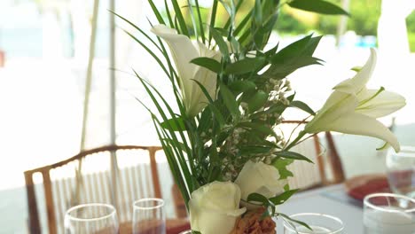 Toma-Panorámica-Lenta-Hacer-Viento-Soplando-Sobre-Flores-Decoración-Del-Lugar-De-La-Boda-Y-Flores-Asientos-Al-Aire-Libre-Playa-De-Arena-Asientos-De-Compromiso-Con-Mesas