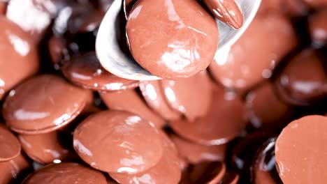 spoon stirring glossy chocolate discs in bowl