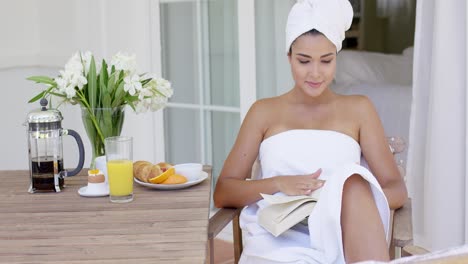 woman in bath towel reading book at table