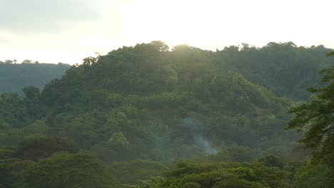 beautiful scenery landscape of the rainforest hills with the sun setting above and smoke coming from the middle of the forest