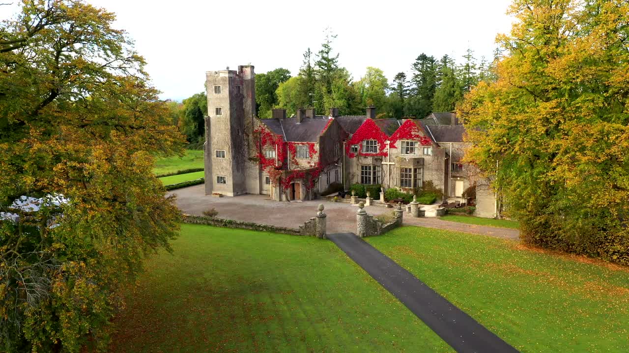 Drone slow approach castle through symmetrical tree lined path with vibrant orange fall tones