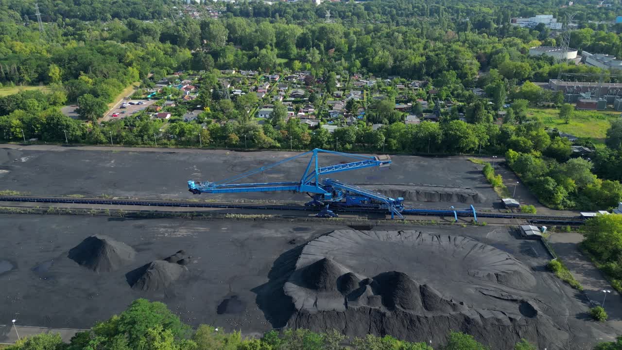 Ekskavator penumpuk batubara di terminal batubara dekat area perumahan. Pemandangan udara menakjubkan dari drone yang terbang di atas.