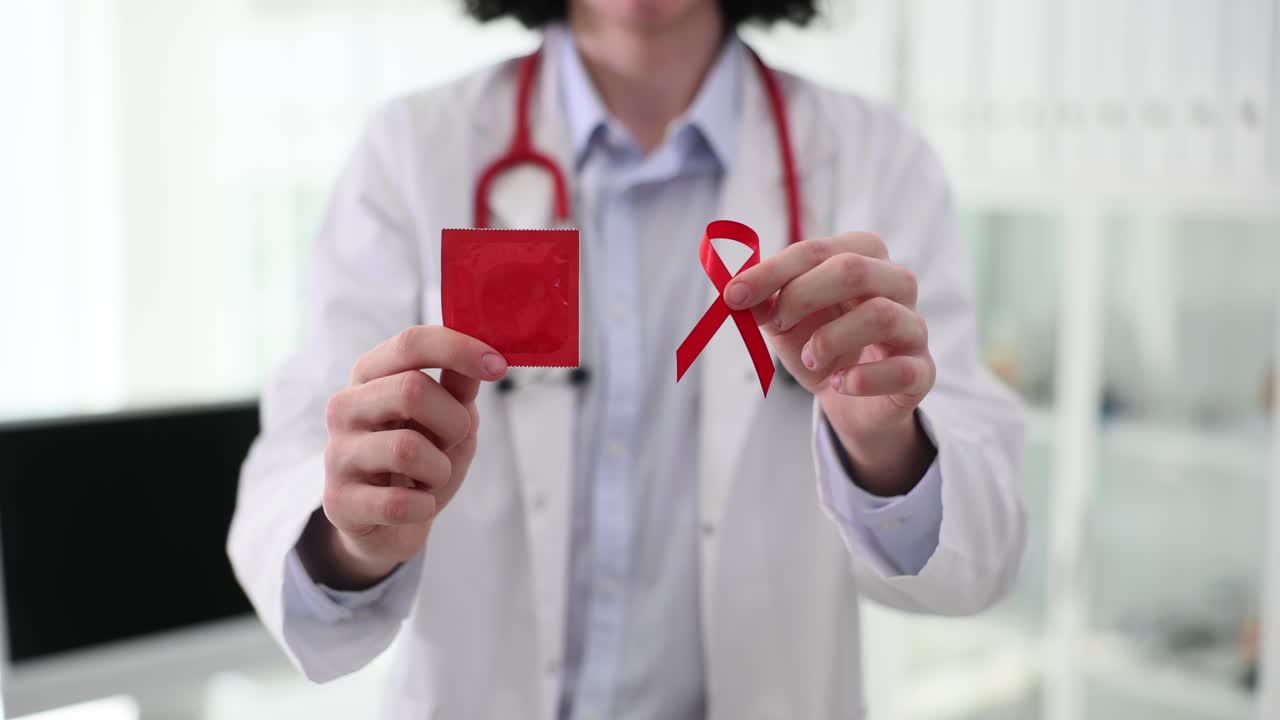 Doctor holding a condom and a red ribbon for AIDS awareness