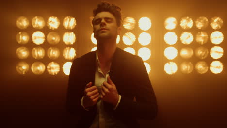 man model straighten jacket standing in spotlights. guy posing in nightclub.