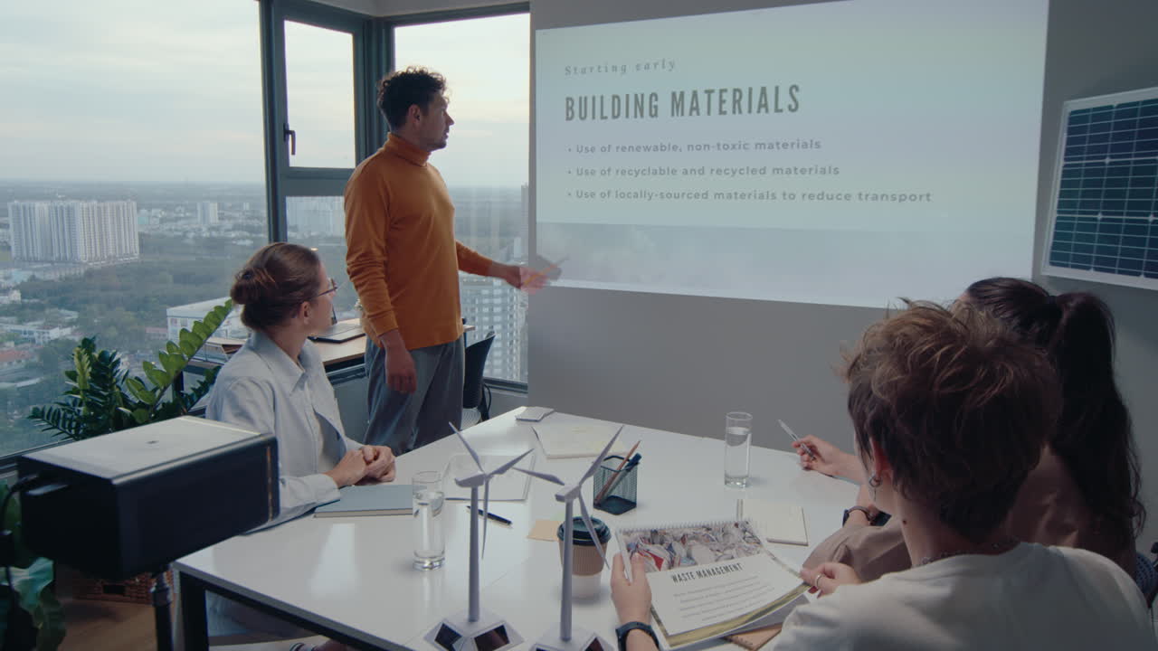 사무실에서 비즈니스 미팅을 하는 동안 여성 동료들에게 지속가능한 개발에 관한 프로젝트를 제시하는 젊은이. , 시내 풍경은 창문 뒤에서 볼 수 있습니다.