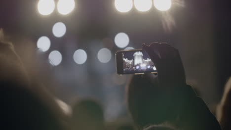 view from behind of hands hold smartphone among people at rave party with light