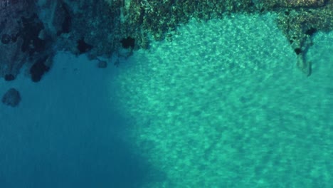 Backward-aerial-of-rugged-coastline-down-to-to-turquoise-clear-water,-tilt-down