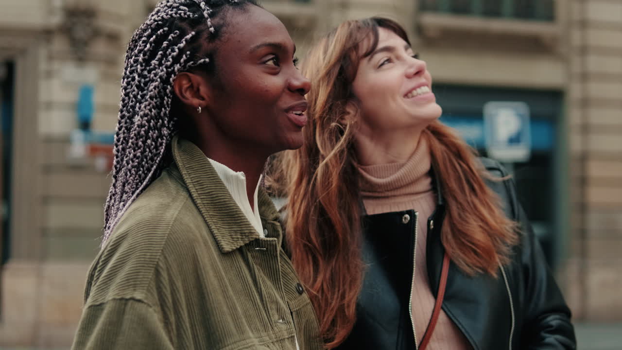 Duas jovens diversas sorrindo e olhando para cima em uma rua da cidade