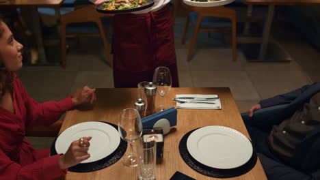 camarero que sirve comida en un restaurante a una pareja multiétnica en una cita romántica.