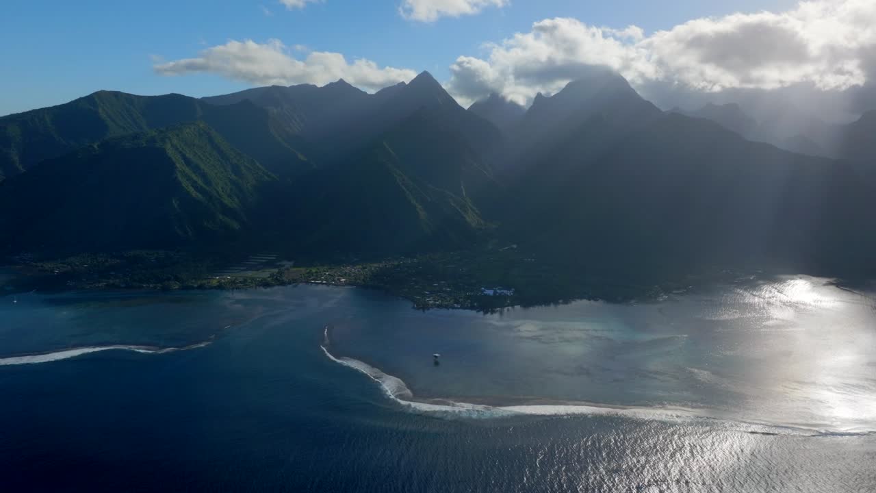 Moorning sun glare clouds reflection Teahupoo Tahiti  aerial drone French Polynesia South Pacific towering mountains peaks coast sunrise surf wave reef channel WSL surfing Olympic venue static shot