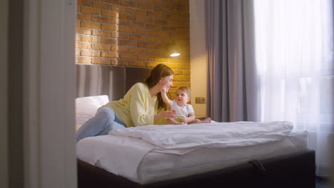 distant view of woman and her baby sitting on the bed at home