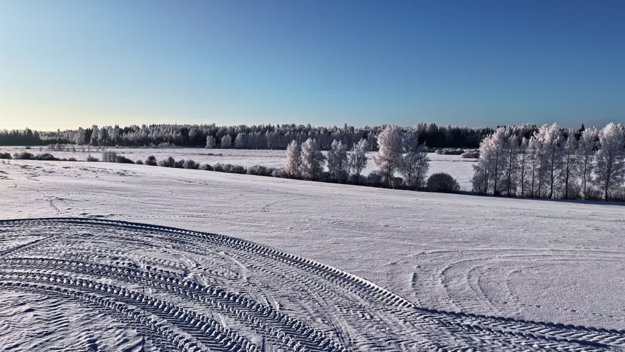 Filmatisk drönarflygning i FPV-stil framåt över en snöig väg och frusna fält i Lettland under en gyllene vinteruppgång.