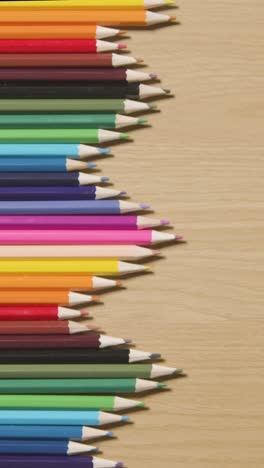 vertical video of coloured pencils arranged in a symmetrical pattern on wooden background