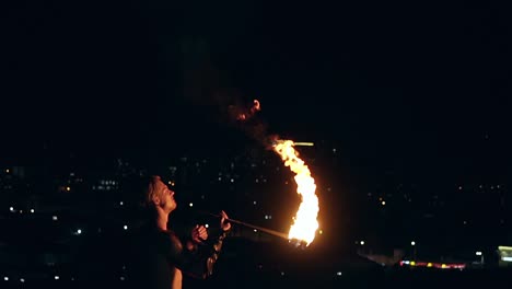 young blond male breathes out large stream of fire with torch on black background slow motion shot