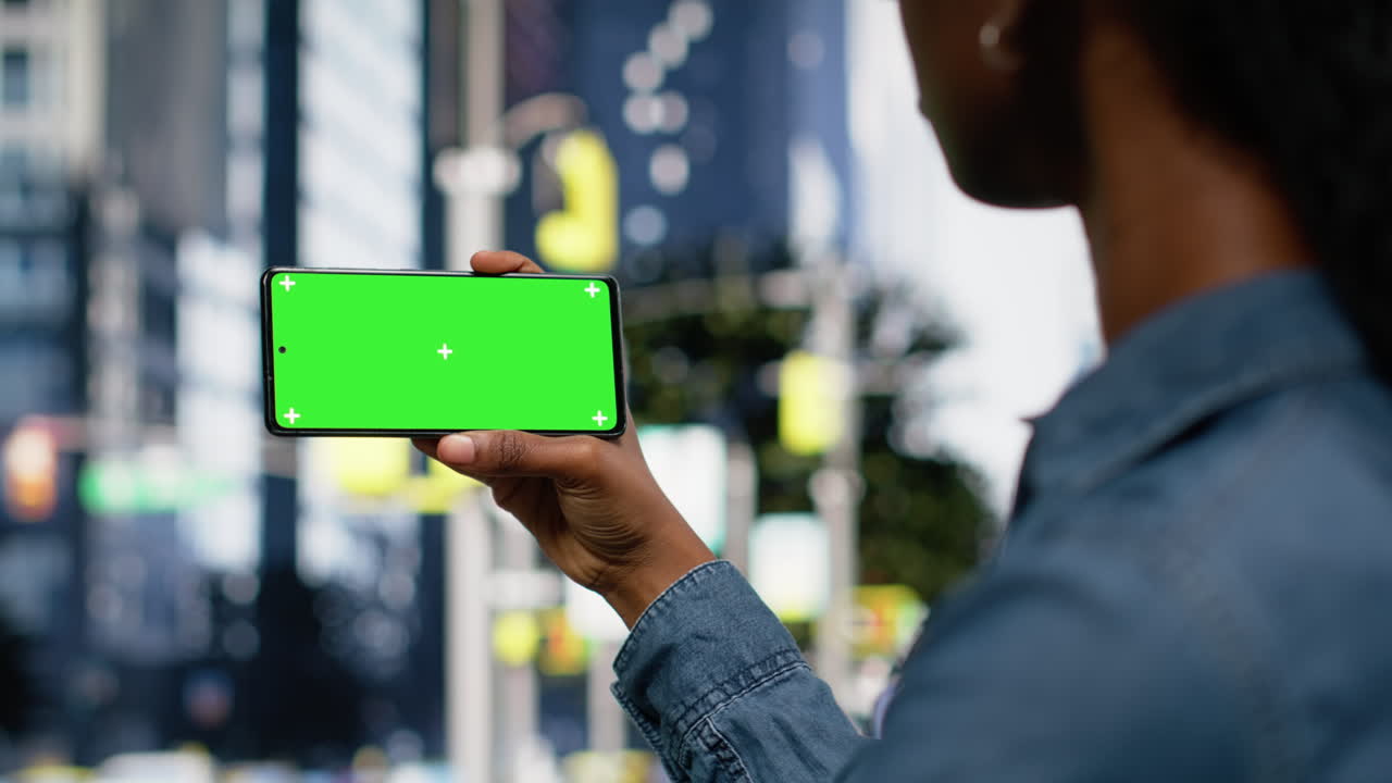 Schermo chroma key su telefono cellulare tenuto da una donna afroamericana in centro città