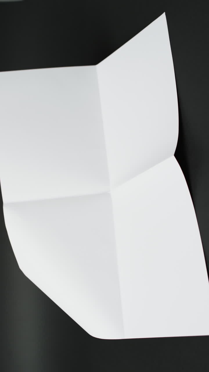 Vertical video of piece of white paper with creases on black background