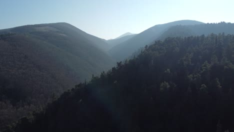 Drone-forward-over-hills-and-forrest-at-national-park-in-Italy,-Marken,-Umbria,-at-sunset-in-early-spring