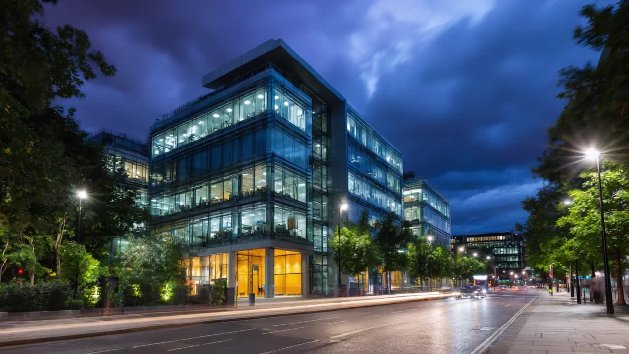 Prédio de escritórios moderno de vidro ao entardecer com janelas iluminadas e luzes da rua refletindo no céu noturno, mostrando o design arquitetônico urbano e a atmosfera.