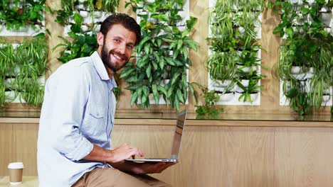 Portrait-male-executive-sitting-on-desk-and-using-laptop