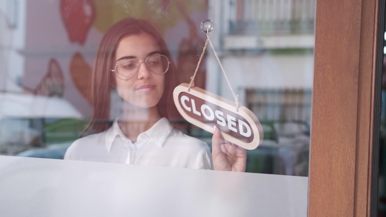 Happy small business girl changing closed to open sign on window smiling looking outside waiting for clients. Start-up concept.