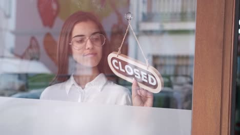 happy small business girl changing closed to open sign on window smiling looking outside waiting for clients. start-up concept.