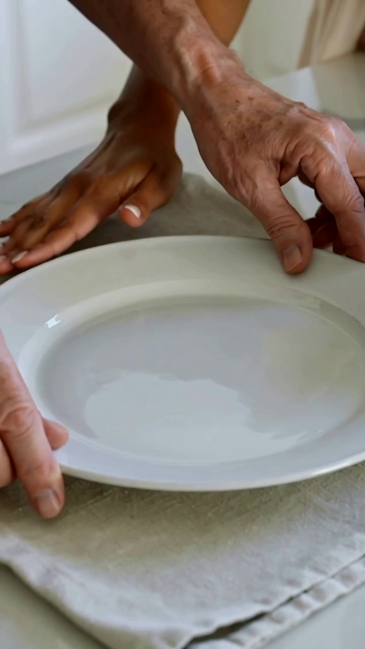 Video verticale: Mani di un anziano che abbassano e stabilizzano un piatto bianco su un panno piegato sul bancone per il pasto.