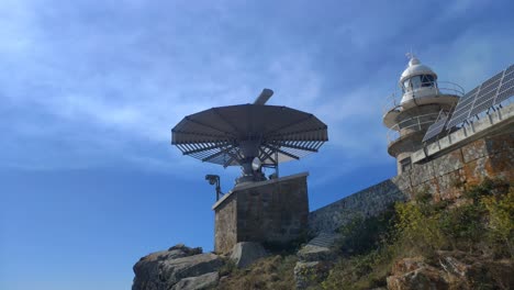 Maritime-traffic-control-radar-next-to-the-lighthouse-with-solar-panels-on-top-of-the-hill-on-a-sunny-summer-day,-shot-blocked-from-below