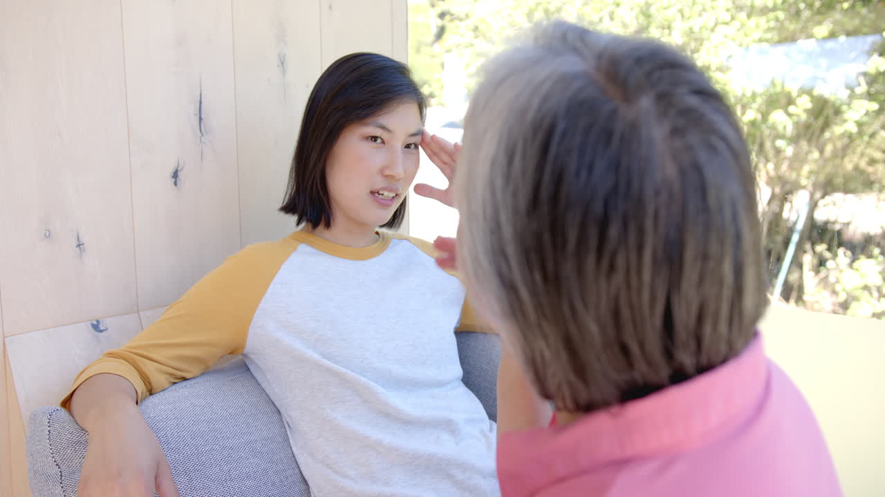 Talking with senior, young asian woman sitting on couch, engaging in conversation