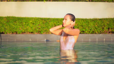 Mujer-Asiática-Delgada-En-Traje-De-Baño-Arreglando-Su-Cabello-Mojado-Después-De-Nadar-En-La-Piscina-De-Un-Resort-De-Lujo